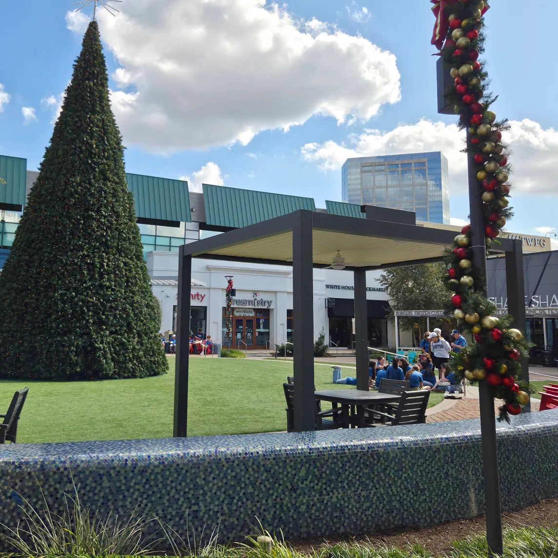 Outdoor plaza with a large artificial Christmas tree, patio seating, and holiday decorations