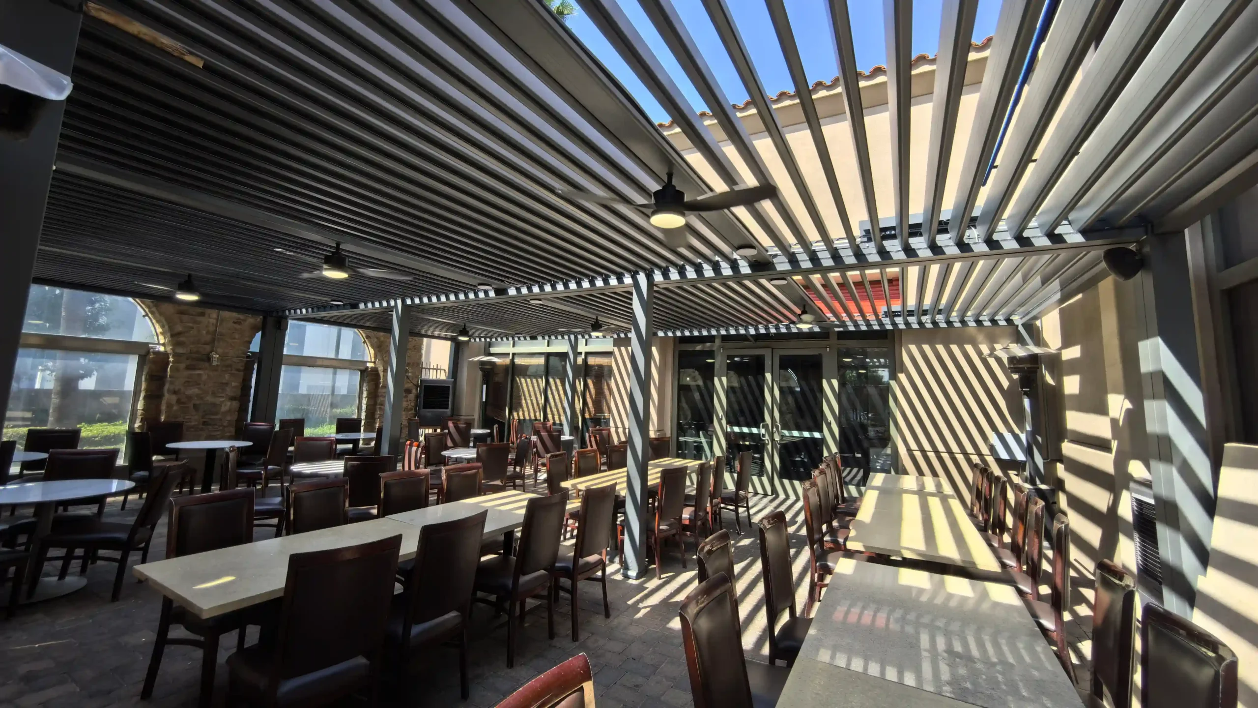 Restaurant outdoor dining area with adjustable louvered roof, tables, and ceiling fans
