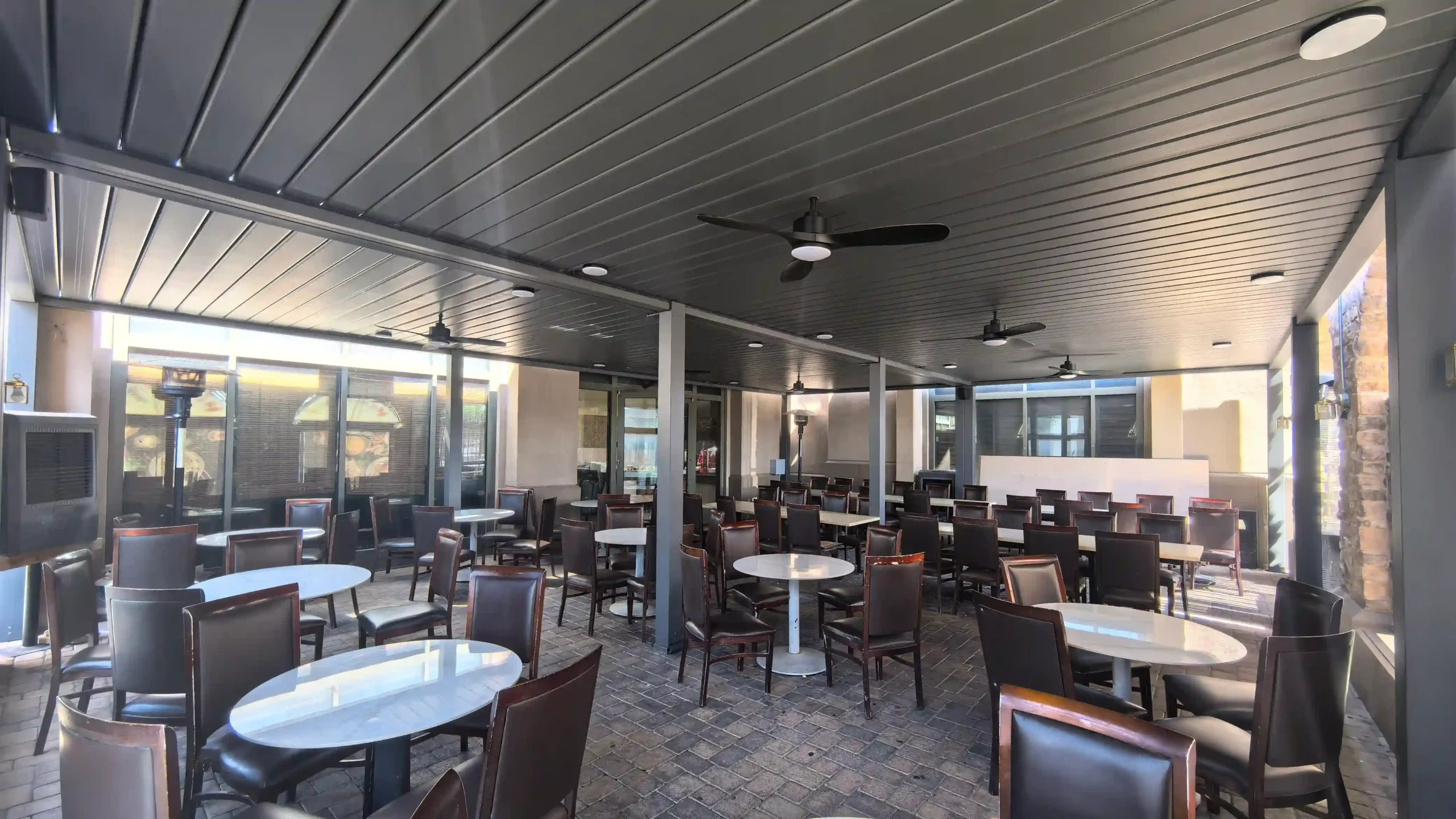 Gray motorized solar aluminum louvered pergola covering commercial restaurant outdoor patio with ceiling fans and dining tables