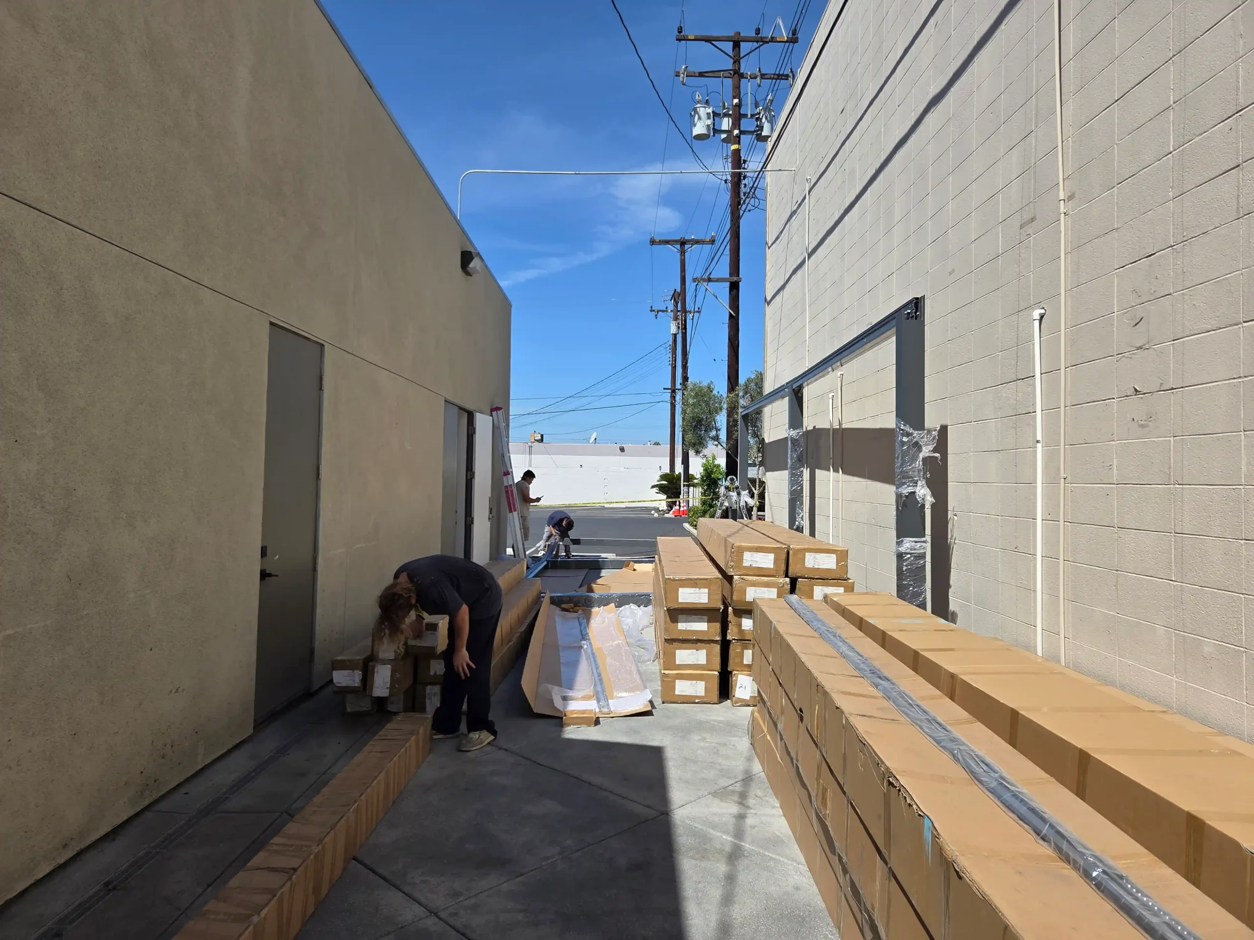 Workers organize and unpack metal frame components from shipping boxes in a narrow alley