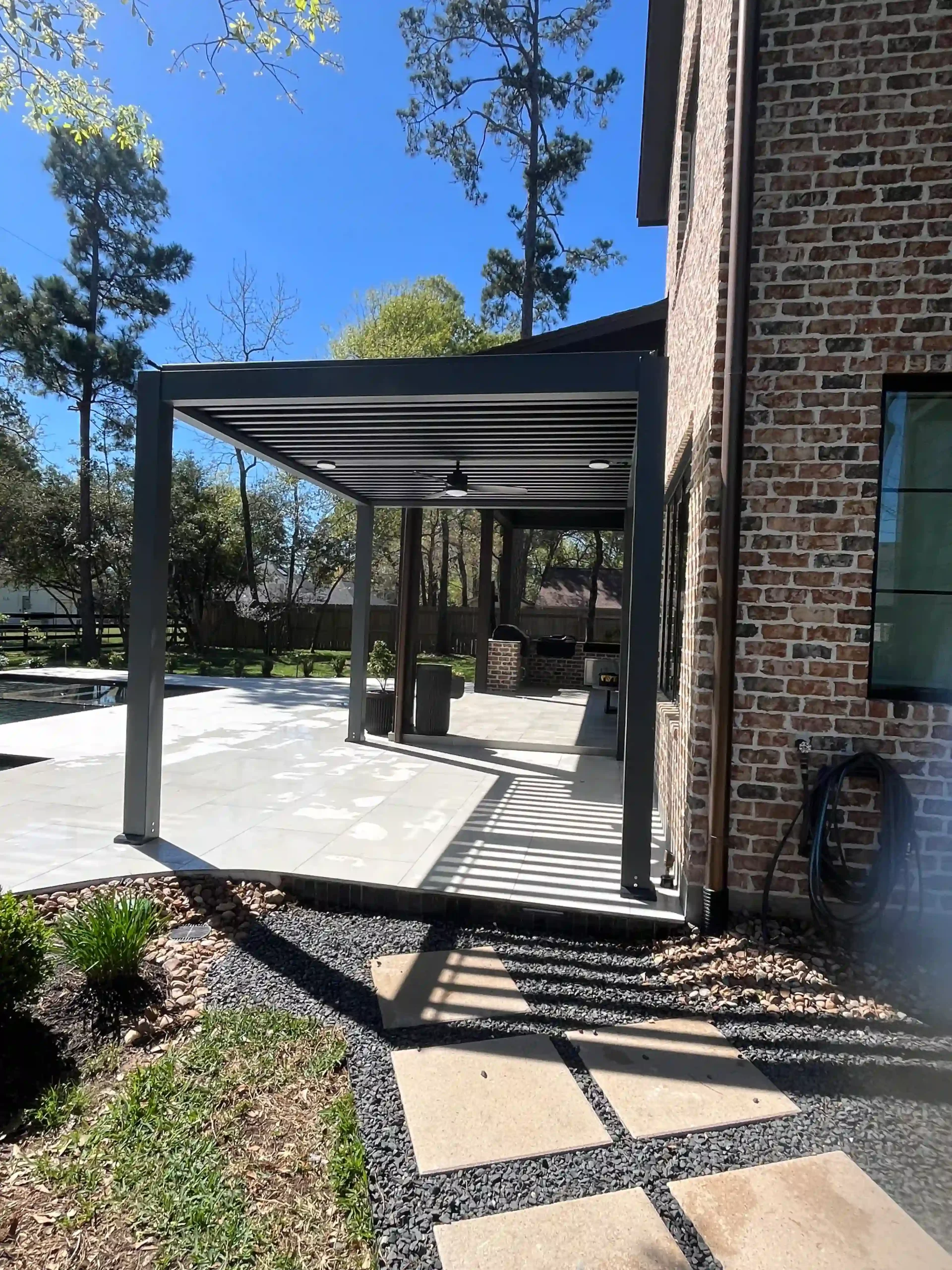 gray freestanding louvered pergola attached to brick home exterior