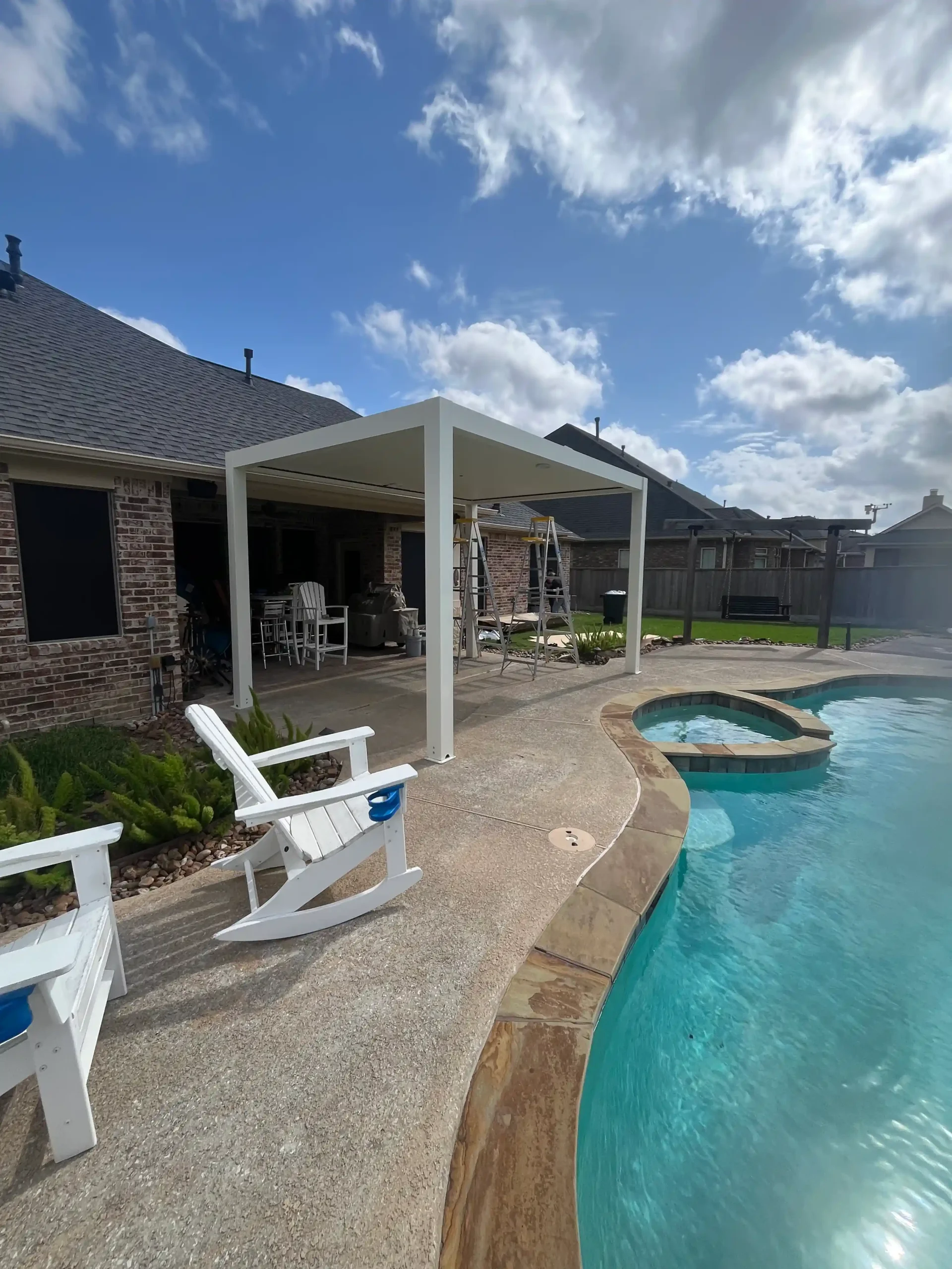 poolside patio with white shade structure and outdoor rocking chairs