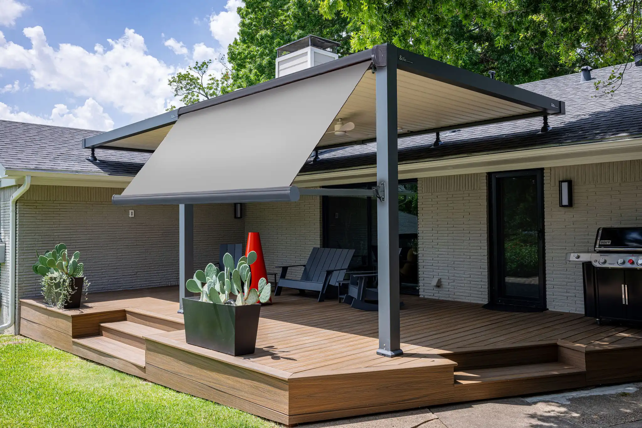 Light gray drop arm awning mounted on a residential backyard pergola, providing shade for a wooden deck patio