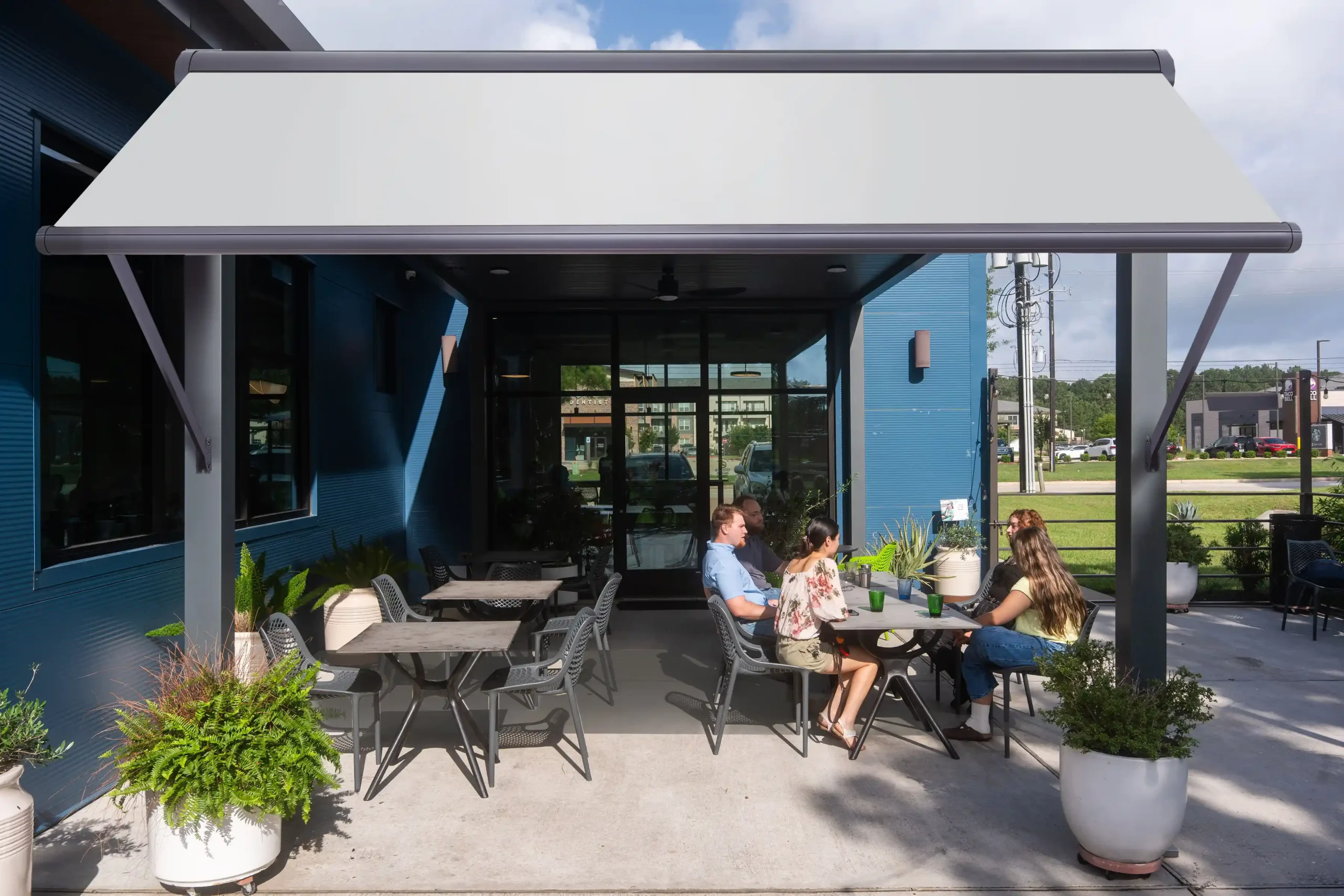 Light gray drop arm awning on a commercial patio pergola, shading outdoor dining space at a modern restaurant