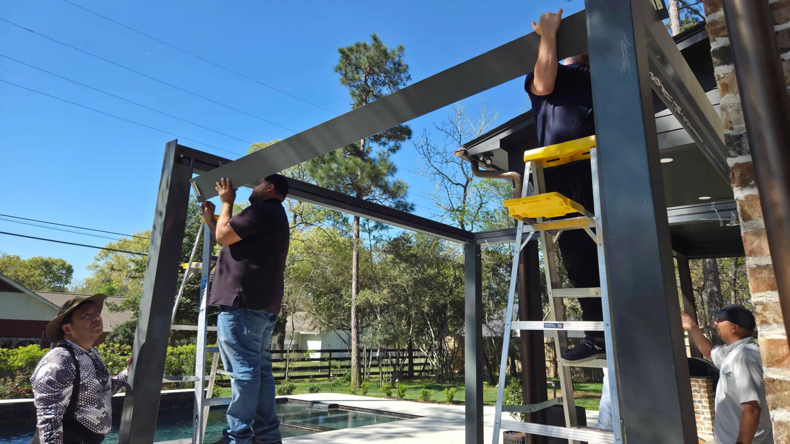 Professional installers assembling an aluminum louvered pergola on a residential backyard patio